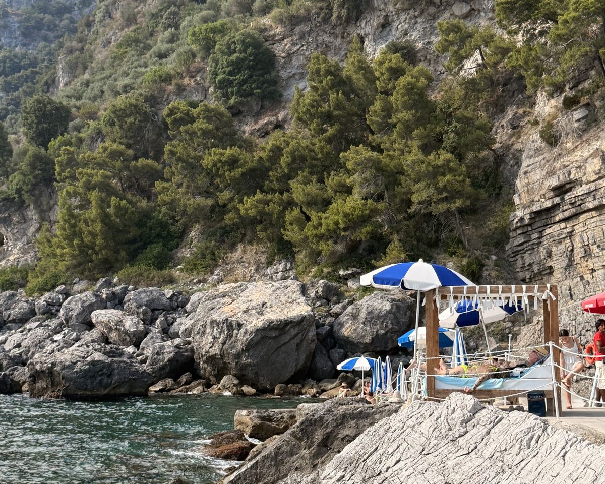 Secluded rocky cove below the cliffs at La Gavitella, with blue and white umbrellas and sunbeds by the sea in Praiano