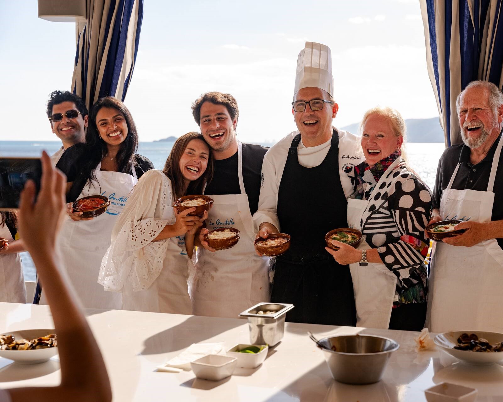 Ospiti sorridenti con il grembiule insieme allo chef mostrano la pasta fatta a mano durante una cooking class a La Gavitella